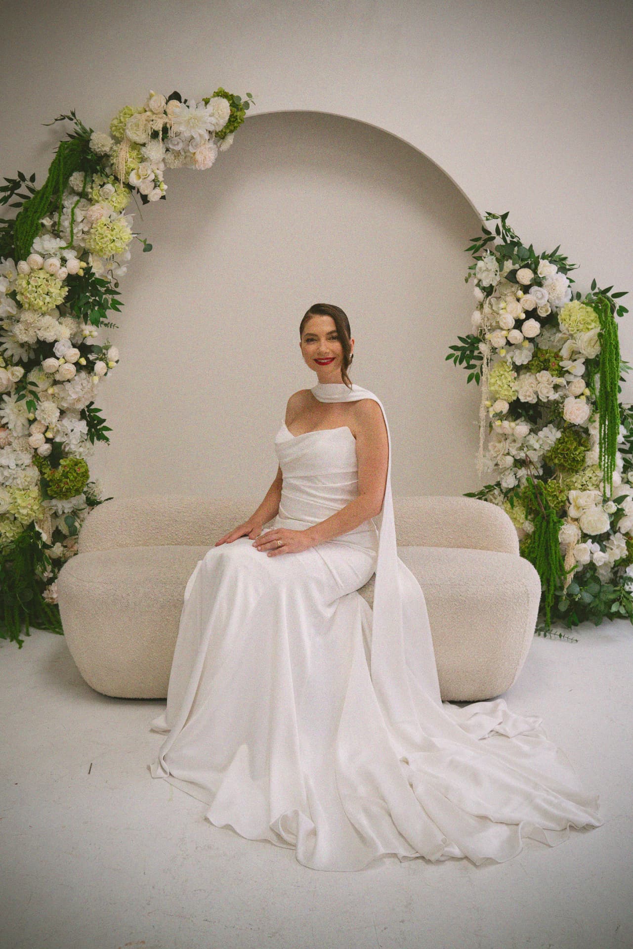 La mariée assise devant une arche de fleurs blanches
